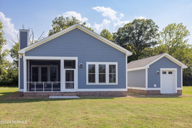 back of property featuring an outbuilding, a lawn, a garage, and a sunroom