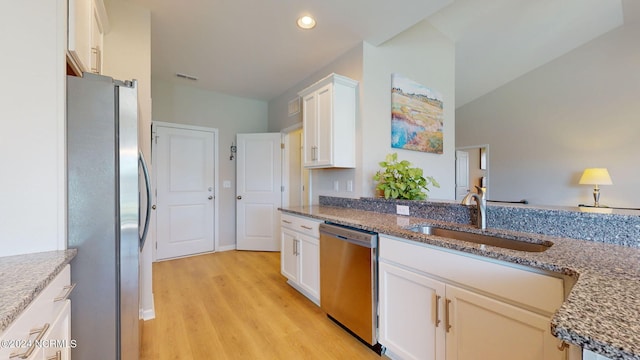 kitchen with sink, dark stone counters, stainless steel appliances, light hardwood / wood-style floors, and white cabinets