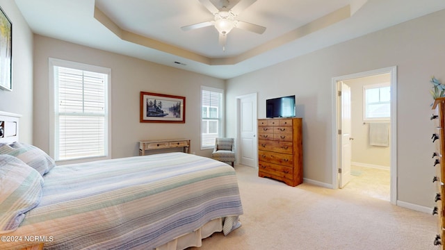 carpeted bedroom with ensuite bathroom, ceiling fan, and a tray ceiling