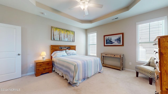 bedroom with light colored carpet, a raised ceiling, and multiple windows