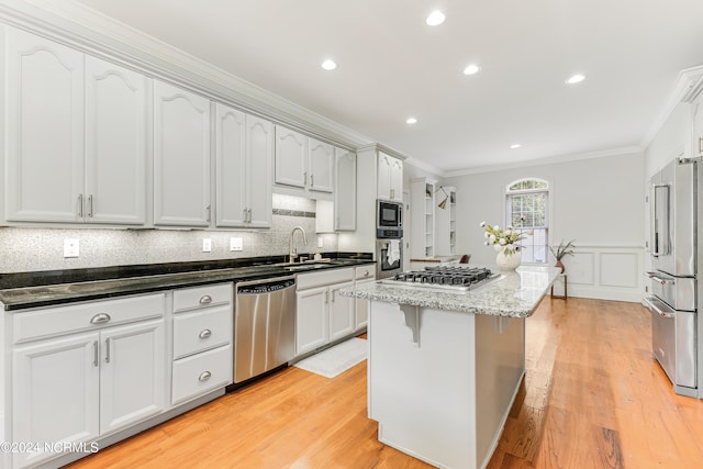 kitchen with appliances with stainless steel finishes, light hardwood / wood-style floors, dark stone countertops, white cabinets, and a center island