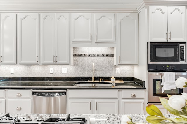 kitchen featuring appliances with stainless steel finishes, decorative backsplash, dark stone countertops, white cabinets, and sink