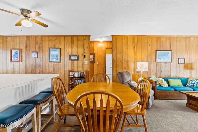 carpeted dining space featuring wood walls, ceiling fan, and a textured ceiling