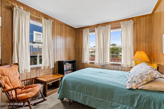 bedroom featuring ornamental molding, wooden walls, a textured ceiling, and carpet flooring