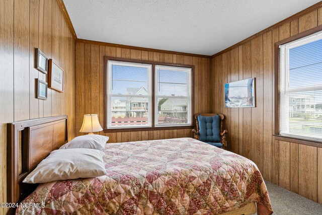 bedroom featuring ornamental molding, wood walls, a textured ceiling, and carpet floors