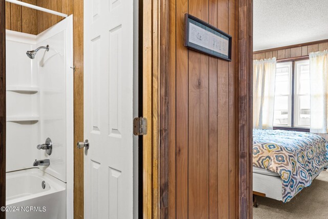 bathroom with a textured ceiling, tub / shower combination, and wooden walls