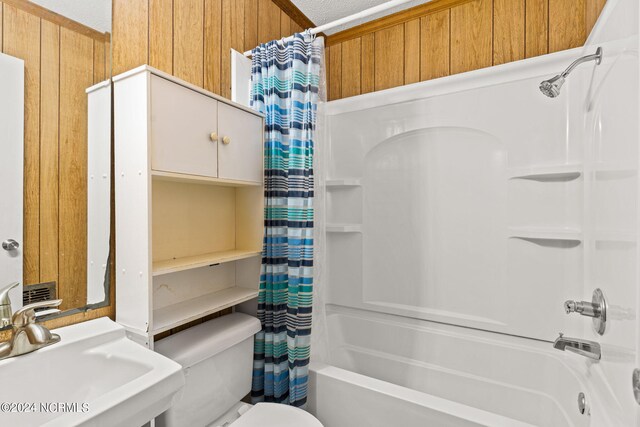 full bathroom featuring shower / bathtub combination with curtain, a textured ceiling, wooden walls, toilet, and sink