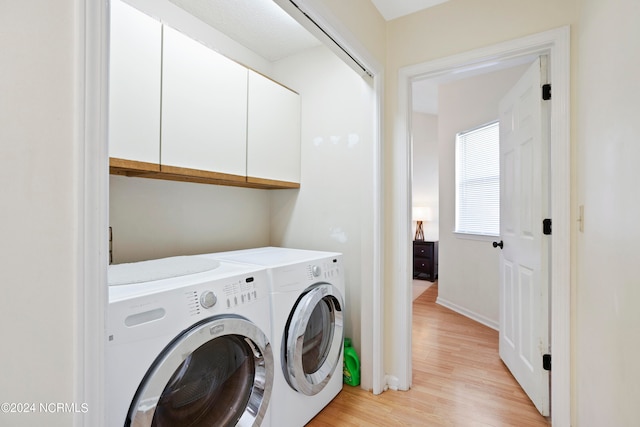 clothes washing area with washer and dryer, light hardwood / wood-style flooring, and cabinets