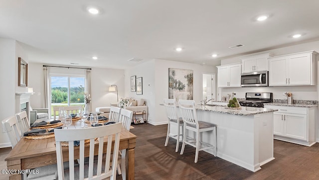 kitchen with light stone countertops, stainless steel appliances, white cabinetry, and a kitchen island with sink