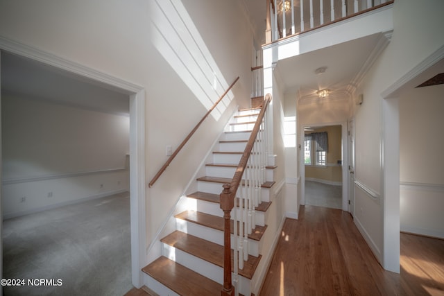 staircase featuring hardwood / wood-style flooring, crown molding, and a high ceiling