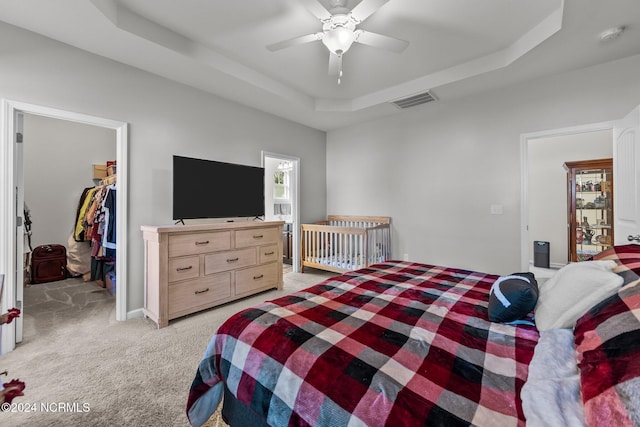 carpeted bedroom with a closet, a spacious closet, a raised ceiling, and ceiling fan