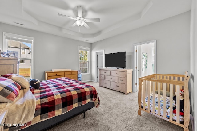 carpeted bedroom with multiple windows, ceiling fan, and a tray ceiling