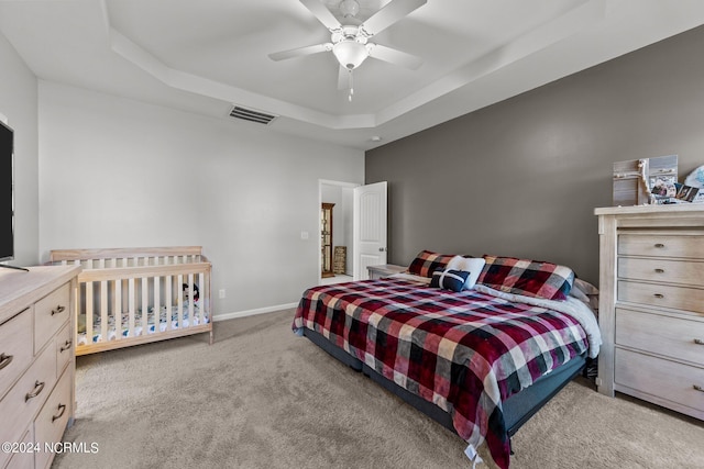 carpeted bedroom with ceiling fan and a raised ceiling