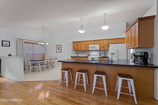 kitchen featuring light hardwood / wood-style flooring, backsplash, a kitchen bar, a chandelier, and white appliances