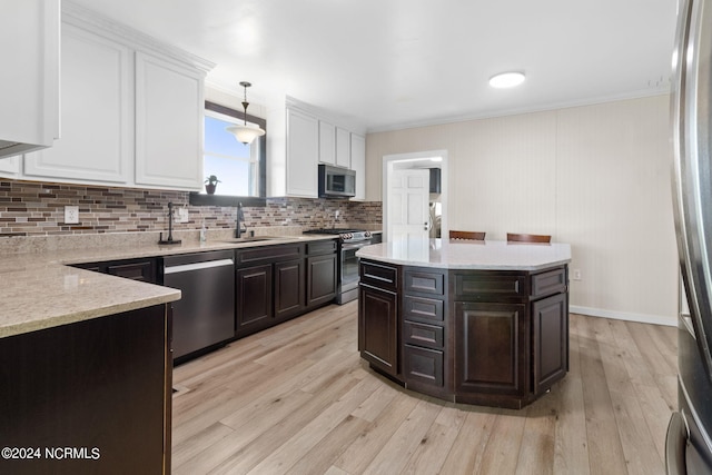 kitchen with appliances with stainless steel finishes, decorative light fixtures, light hardwood / wood-style flooring, and ornamental molding