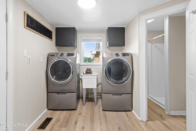 clothes washing area with washer and clothes dryer, light hardwood / wood-style floors, and cabinets