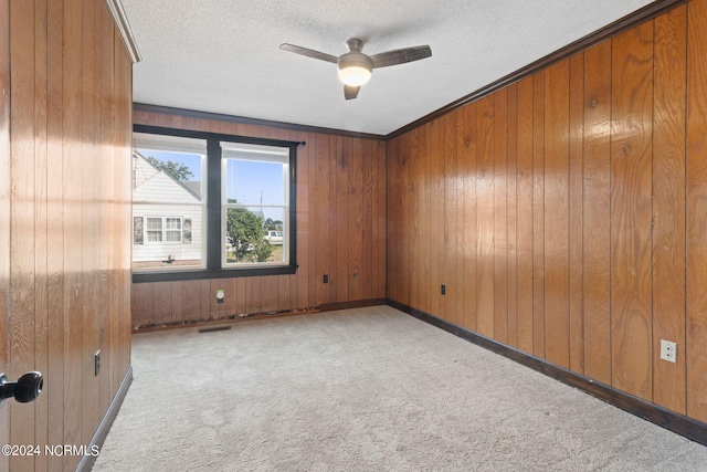 carpeted empty room featuring a textured ceiling, ceiling fan, wood walls, and ornamental molding