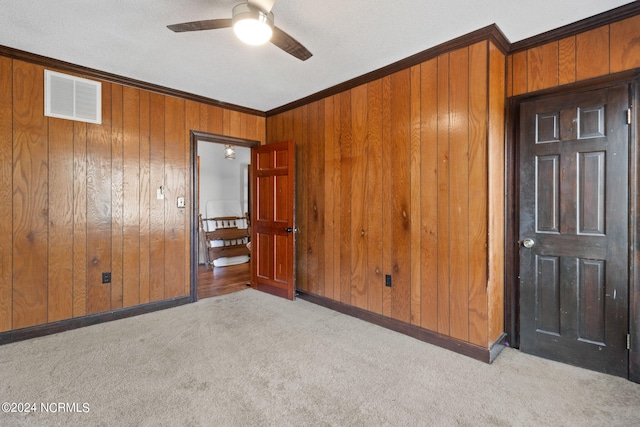 spare room featuring wooden walls, ceiling fan, ornamental molding, a textured ceiling, and light colored carpet