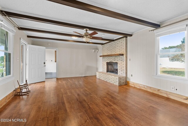 unfurnished living room with hardwood / wood-style floors, a fireplace, a wealth of natural light, and beamed ceiling