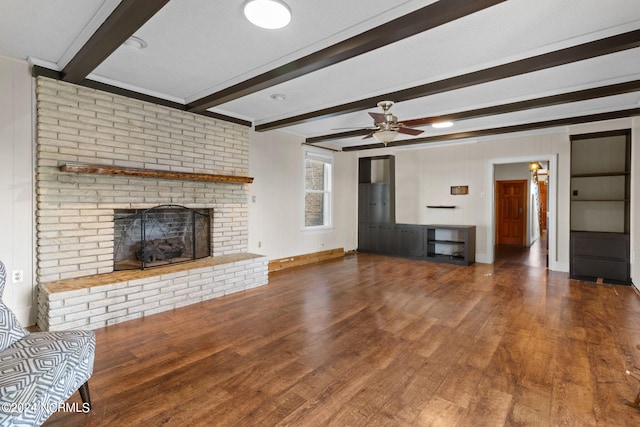 unfurnished living room with beam ceiling, ceiling fan, dark wood-type flooring, and a brick fireplace