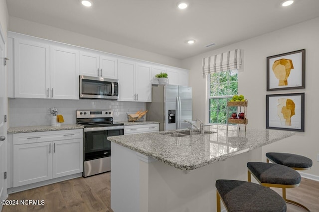 kitchen with light hardwood / wood-style flooring, stainless steel appliances, white cabinetry, sink, and a kitchen island with sink