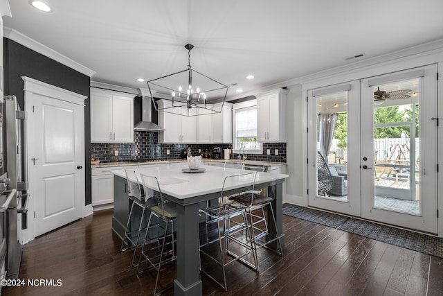 kitchen featuring a healthy amount of sunlight, a kitchen island, dark wood-type flooring, and wall chimney range hood