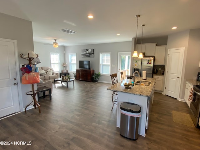 kitchen with a kitchen island with sink, plenty of natural light, decorative light fixtures, and stainless steel fridge