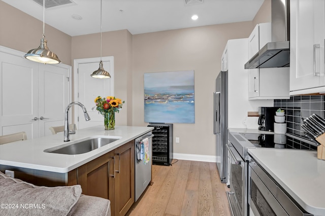 kitchen featuring white cabinets, sink, wall chimney exhaust hood, an island with sink, and appliances with stainless steel finishes