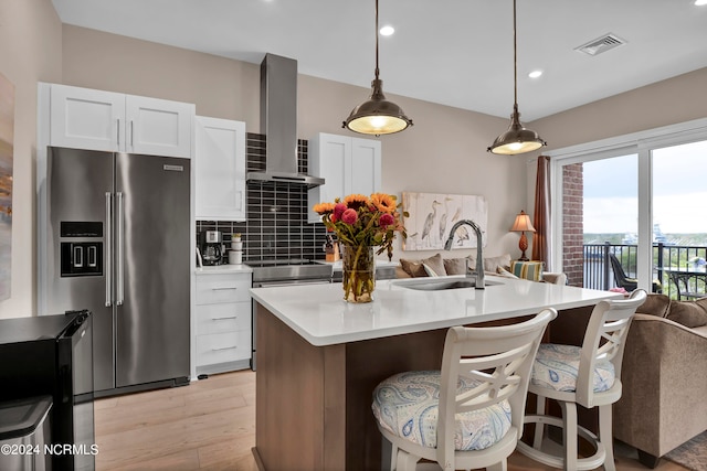 kitchen with white cabinetry, sink, stainless steel appliances, wall chimney range hood, and a kitchen island with sink