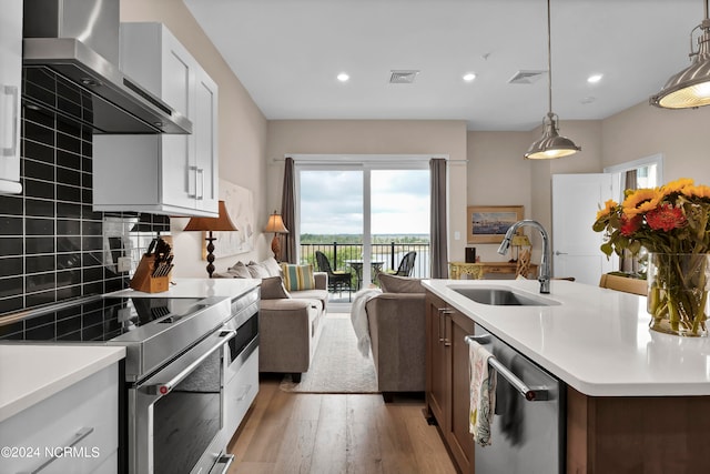 kitchen featuring white cabinetry, sink, wall chimney exhaust hood, decorative light fixtures, and appliances with stainless steel finishes