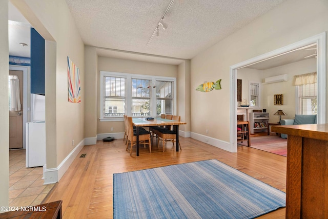 dining area featuring a wall unit AC, a textured ceiling, light wood-type flooring, and rail lighting