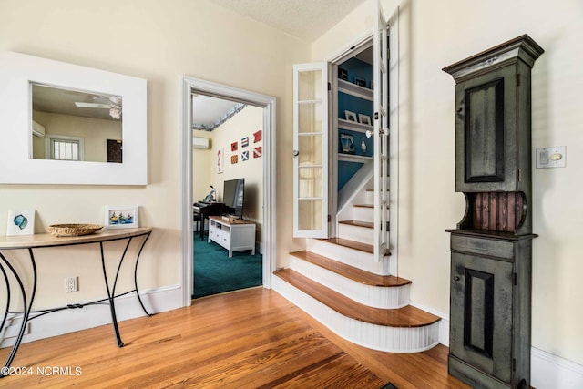 interior space featuring a fireplace, a textured ceiling, ceiling fan, hardwood / wood-style floors, and a wall mounted AC