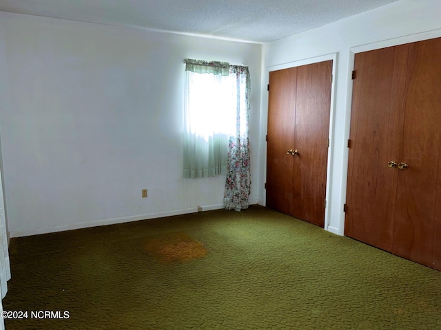 unfurnished bedroom featuring multiple closets, a textured ceiling, and dark carpet