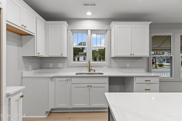 kitchen featuring light stone counters, sink, and white cabinets