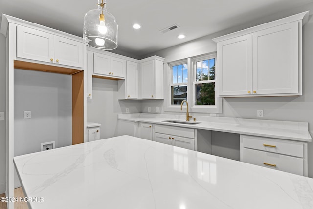 kitchen with light stone countertops, decorative light fixtures, sink, and white cabinetry