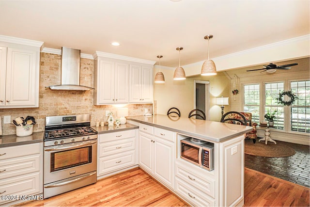 kitchen featuring appliances with stainless steel finishes, kitchen peninsula, light wood-type flooring, and wall chimney range hood