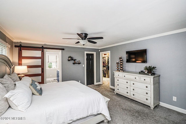 bedroom featuring a barn door, carpet, a walk in closet, ornamental molding, and ceiling fan