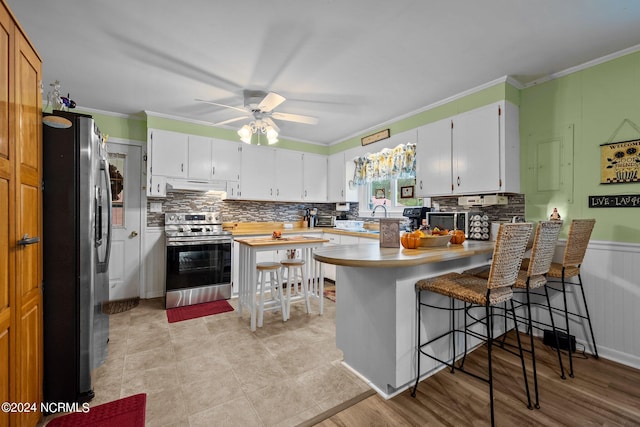 kitchen featuring ceiling fan, white cabinets, kitchen peninsula, stainless steel appliances, and a breakfast bar