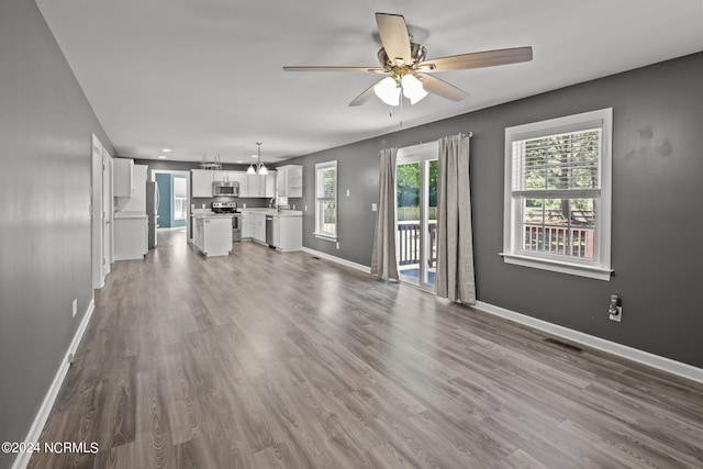 unfurnished living room featuring wood-type flooring, ceiling fan with notable chandelier, and sink