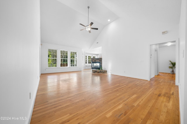 unfurnished living room featuring ceiling fan, light hardwood / wood-style floors, a stone fireplace, and high vaulted ceiling