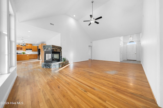 unfurnished living room featuring ceiling fan, a stone fireplace, high vaulted ceiling, and light hardwood / wood-style flooring