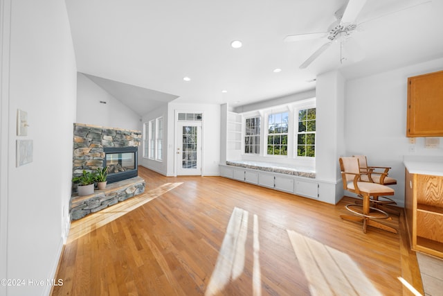 living room with vaulted ceiling, light hardwood / wood-style floors, a stone fireplace, and ceiling fan