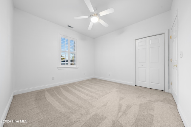 unfurnished bedroom with ceiling fan, light carpet, and a closet