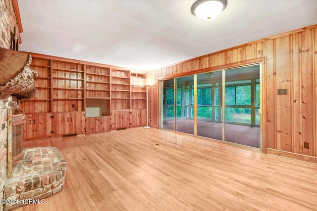 unfurnished living room with wood-type flooring, built in shelves, a fireplace, and wooden walls