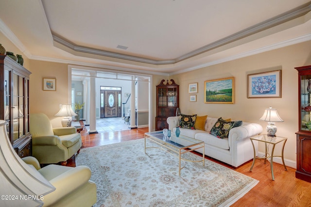 living room featuring ornamental molding, a tray ceiling, light hardwood / wood-style floors, and ornate columns