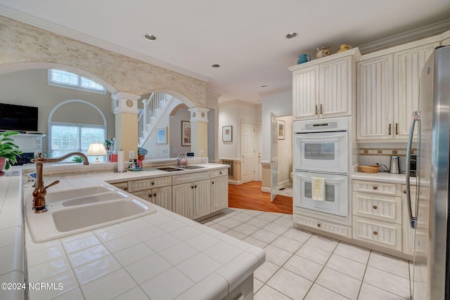 kitchen featuring sink, stainless steel refrigerator, white double oven, tile countertops, and ornate columns