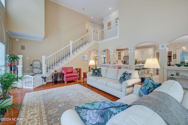 living room with crown molding, decorative columns, arched walkways, wood finished floors, and stairs