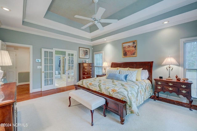 bedroom with ceiling fan, ornamental molding, french doors, hardwood / wood-style flooring, and a tray ceiling