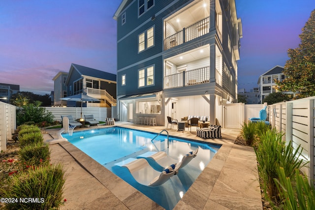 pool at dusk with an outdoor living space and a patio