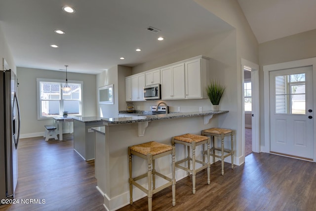 kitchen featuring appliances with stainless steel finishes, a breakfast bar, pendant lighting, white cabinets, and light stone countertops